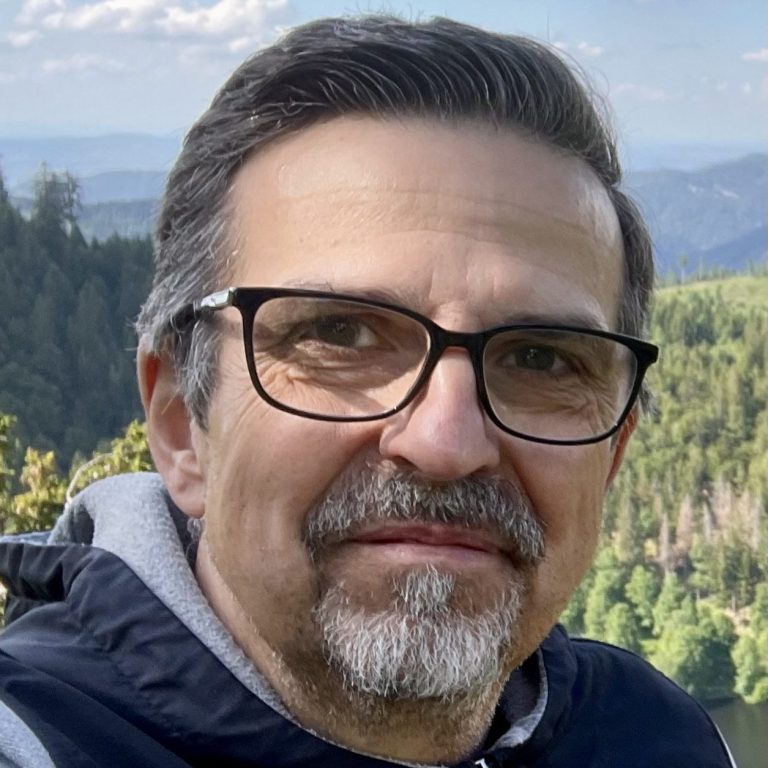 Matthias Figiel Mann mit Brille in Naturkulisse, Blick auf bewaldete Hügel und Himmel.